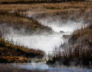 Bendy river with steam coming through a field