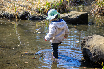 冬の公園の池の中を裸足で歩く男の子
