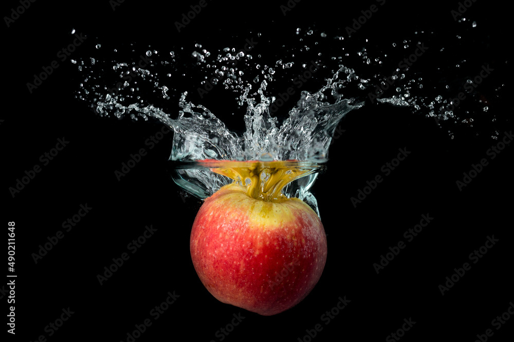 Wall mural Closeup of a red ripe apple dropped into the water with droplets against the black background