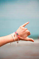 Vertical shot of a hand with bracelets doing a hang loose sign on a beach