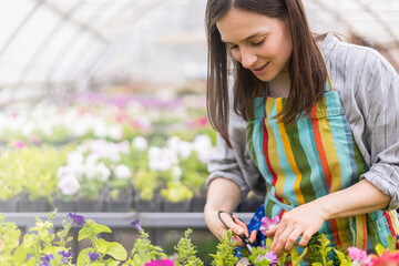 Cheerful female florist pouring fresh water on floral flowerbed with multicolored leaves and petals