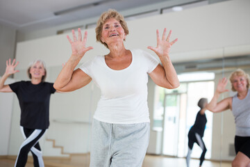 Group of three mature women performing modern dance in exercise room.