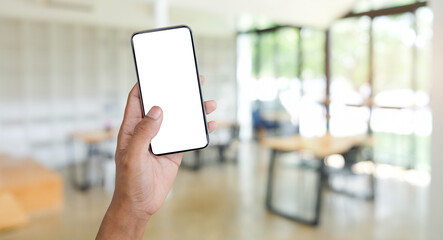 Man hands holding mock up smart phone with blurred coffee shop background. Blank screen for graphic display montage.
