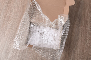 Bubble wrap and foam peanuts in cardboard box on wooden table, above view