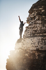 Fototapeta premium Im king of the world. Shot of a young man standing on a mountain cliff with his arms raised.