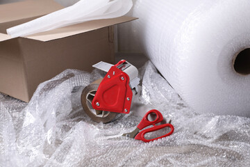 Adhesive tape with bubble wrap, scissors and cardboard box on table