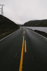 Abwaschbare Fototapete Schwarz Vertikale Aufnahme einer schmalen, leeren Straße auf dem Land neben einem See