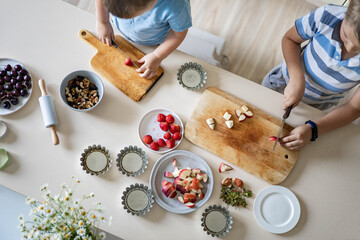 Two cute brothers cooking fresh summer dessert with fruits and berries on kitchen table