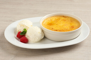 Delicious creme brulee served with scoops of ice cream, fresh raspberries and mint on light wooden table