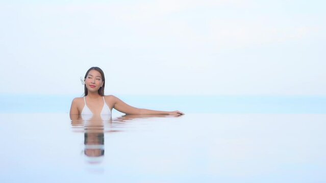 A sexy young woman is resting along the edge of an invisible-edged pool slowly turns her head from three-quarters to profile to look at a Title space.