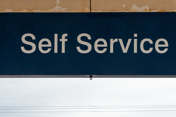 A black and white sign with the text self service. The sign backing is black and the letters are...