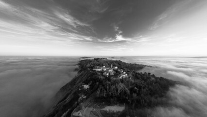 Bird's eye view of the village of Casteldimezzo and Mount San Bartolo covered with fog in grayscale