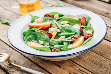 Healthy summer salad with spinach, peach, pecan nuts, blue cheese on wooden table
