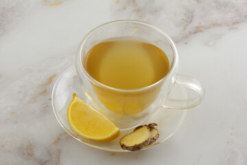 Ginger lemon tea with fresh lemon and ginger slices in insulated glass teacup with saucer