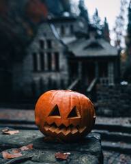 Vertical shot of a jack-o-lantern against a spooky house - Halloween theme