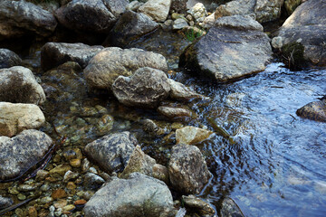 Closeup of a rocky water stream flowing down under a bright sunlight
