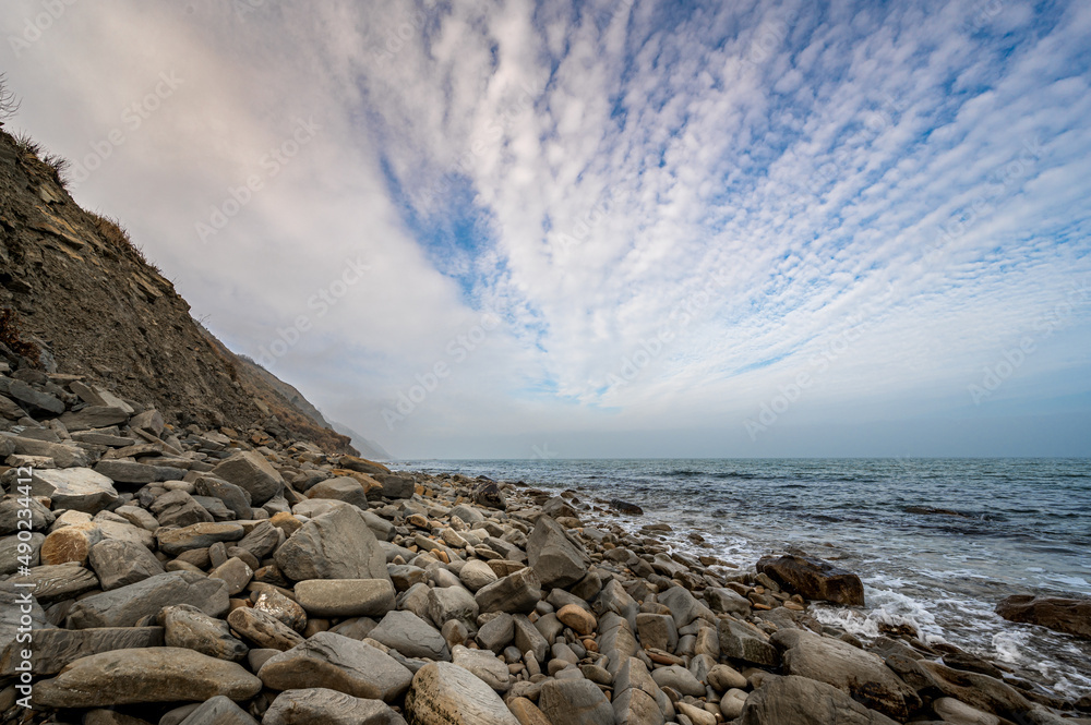 Poster beautiful photo of beach with pebbles, cliff, sea and cloudy sky