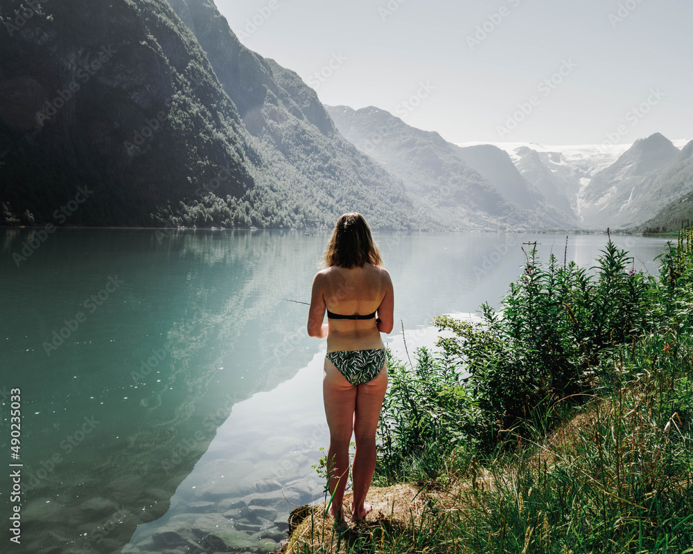 Sticker Woman in a green swimsuit standing on the coast and admiring the mesmerizing views of the seascape