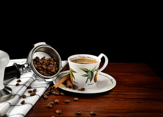Splashed coffee beans from a portafilter on table cloth next to a cup of espresso on a white plate