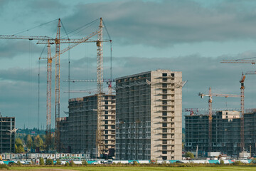 Construction site with industrial building cranes, multi-storey buildings of new city districts and large green field. Blue sky with clouds. Project of urban area.