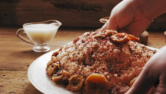 A woman's hand puts a plate of couscous with dried fruits and nuts on the table