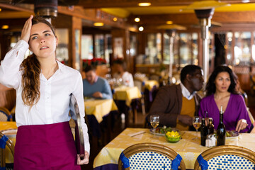 Portrait of tired young caucasian waitress with tray standing in restaurant.