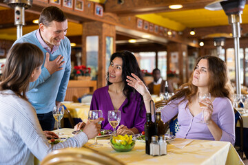 Man having conversation with women who sitting at table and dining in restaurant.