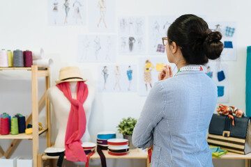 Female fashion designer near paper sheet with drawings hanging on wall in modern office. back view...
