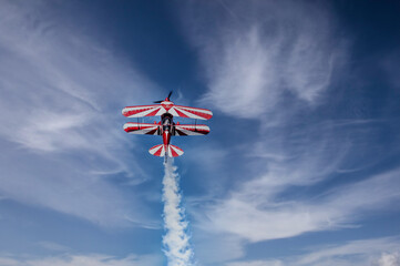 Red and white biplane flying against a blue sky