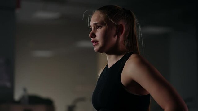 young motivated and tired sportswoman in training hall in evening, female athlete is breathing hard