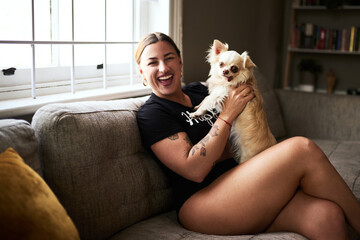 Isnt he just adorable. Cropped portrait of an attractive young woman smiling while holding her dog in her living room at home.