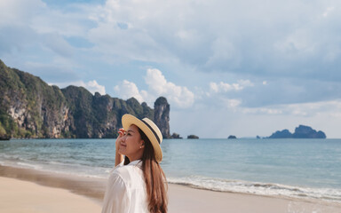 Portrait image of a beautiful young asian woman strolling on the beach with the sea and blue sky...