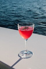 bright pink magenta rosemary beet cocktail on white deck of boat by blue water