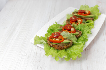 Sandwiches with rye bread, tomatoes, avocados, peppers and spicy sauce on a white plate covered with lettuce. Diet breakfast. healthy eating. Vegan snack Side view, close-up