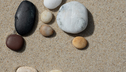 A collection of beach pebbles on the sand with space for copy