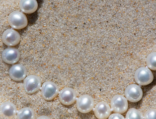 Closeup of a string of pearls in the sand with space for copy