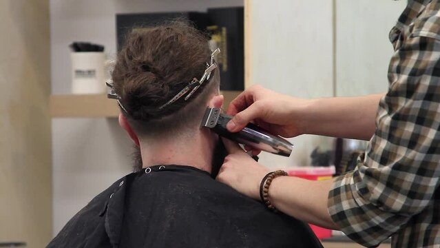 Stylist with trimmer edges hairline of bearded customer with undercut