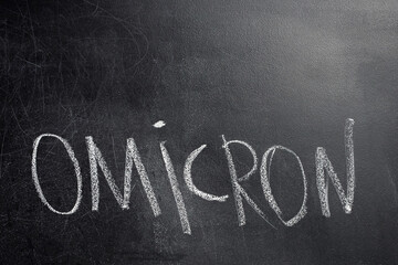 A close-up of the word Omicron written in white chalk on the black board. Omicron is one of the variants of Covid-19. Place to insert text.