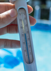Close-up of a man holding a thermometer to measure the temperature of the pool water. The...