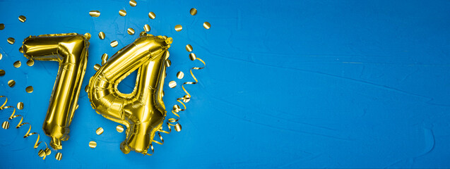 golden yellow foil balloon on blue concrete background number seventy four. Birthday or anniversary card with 74 inscription. Anniversary celebration.