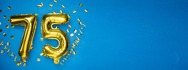golden yellow foil balloon on blue concrete background number seventy five. Birthday or anniversary card with the inscription 75. Anniversary celebration.