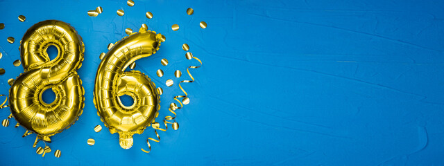 golden yellow foil balloon on blue concrete background number eighty six. Birthday or anniversary...
