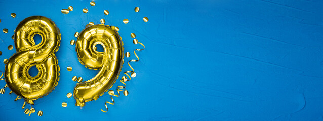 golden yellow foil balloon on blue concrete background number eighty nine. Birthday or anniversary card with 89 inscription. Anniversary celebration.