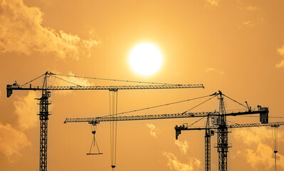 Silhouettes of tower construction cranes with yellow sky at morning time