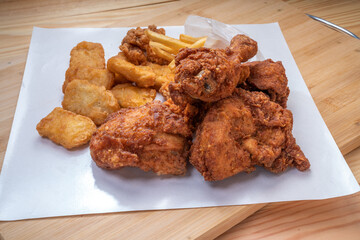 Fried chicken Soft Chicken on white paper with nuggets and french fries on wooden table.