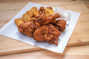 Fried chicken Soft Chicken on white paper with nuggets and french fries on wooden table.