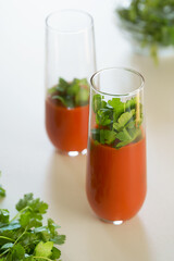 tomato juice with parsley and cucumber in glass glasses on a light background