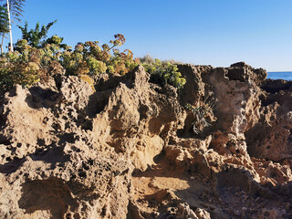 Long frozen lava, the porous shore of the Mediterranean Sea against the background of a blue cloudless sky and water.