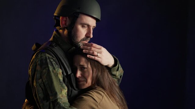 Sad woman hugging her military husband and saying-goodby to him before going to army on black backgound.