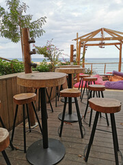 Cafe next to the beach. Tables and bar stools made from sawn wood, a tent with soft, low mattresses, scattered multi-colored pillows and decorative lanterns
